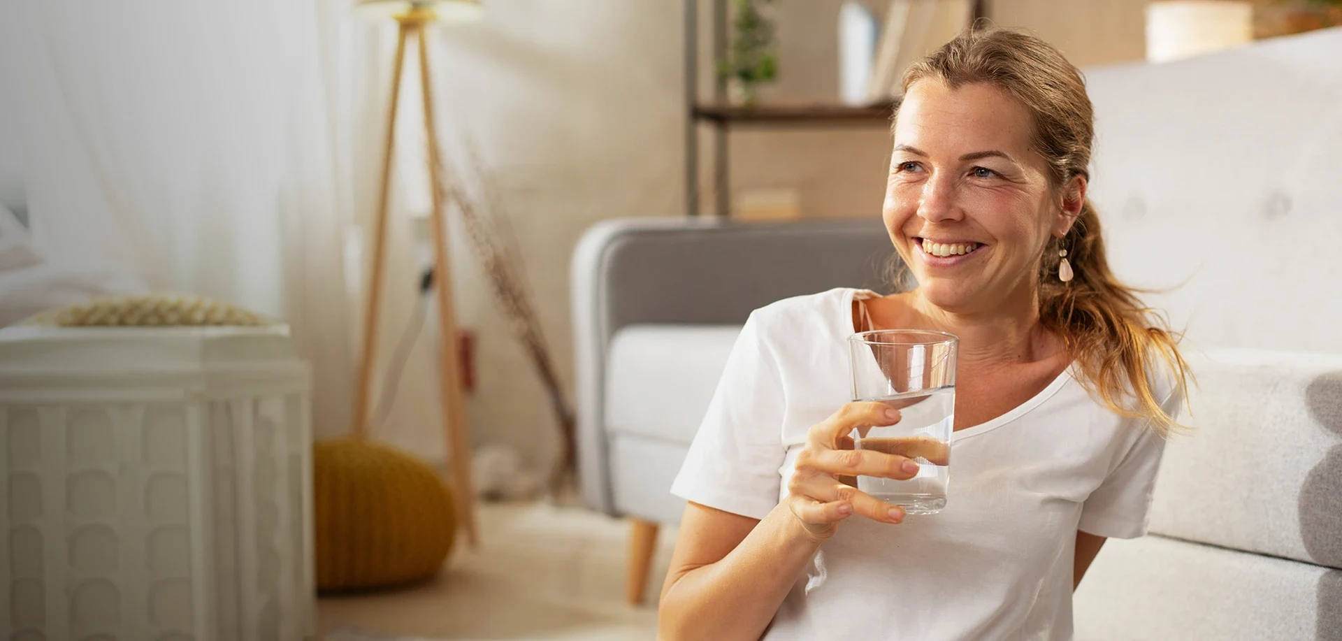 Une femme rit en buvant un verre d’eau dans le salon