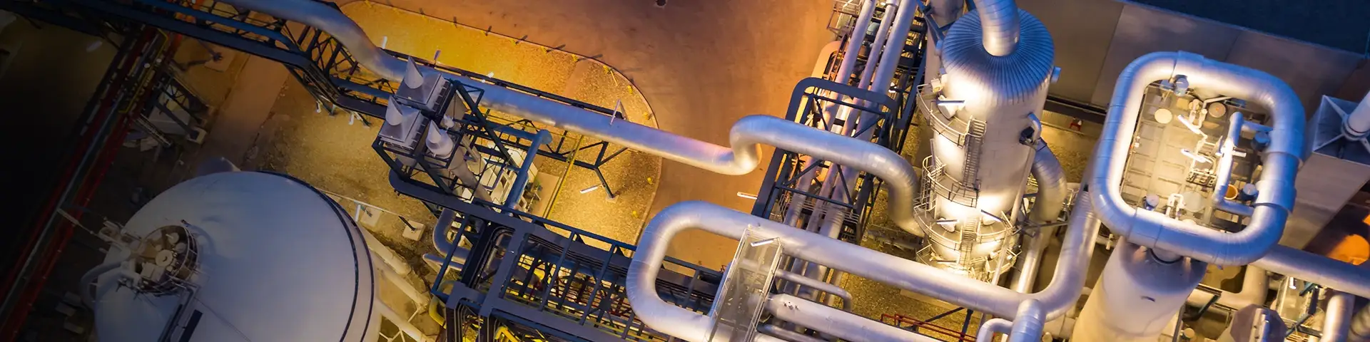 Vue aérienne nocturne d'une installation industrielle avec tuyaux et réservoirs éclairés.