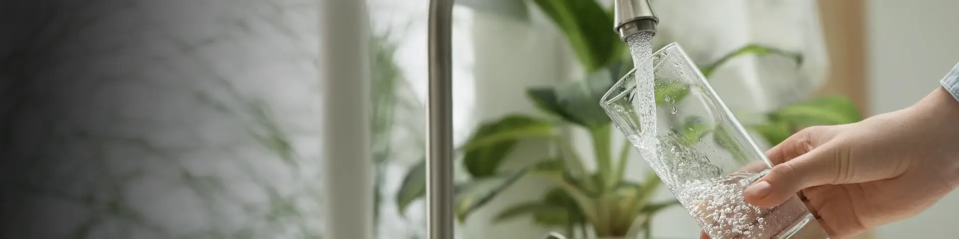 Hand vult glazen karaf met water uit moderne keukenkraan