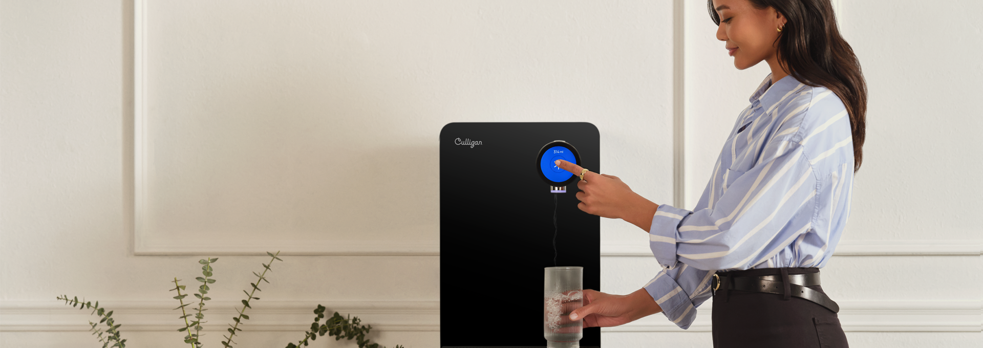 Vrouw schenkt water in een glas uit een moderne waterdispenser, met planten op de achtergrond